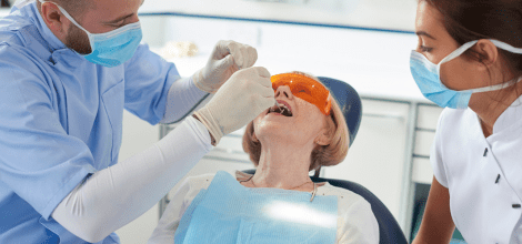 young white male dentist and white female assistant treating a white elderly female patient in a dental practice